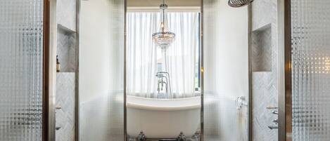 A luxurious bathroom with a freestanding bathtub, a modern shower, and a chandelier.