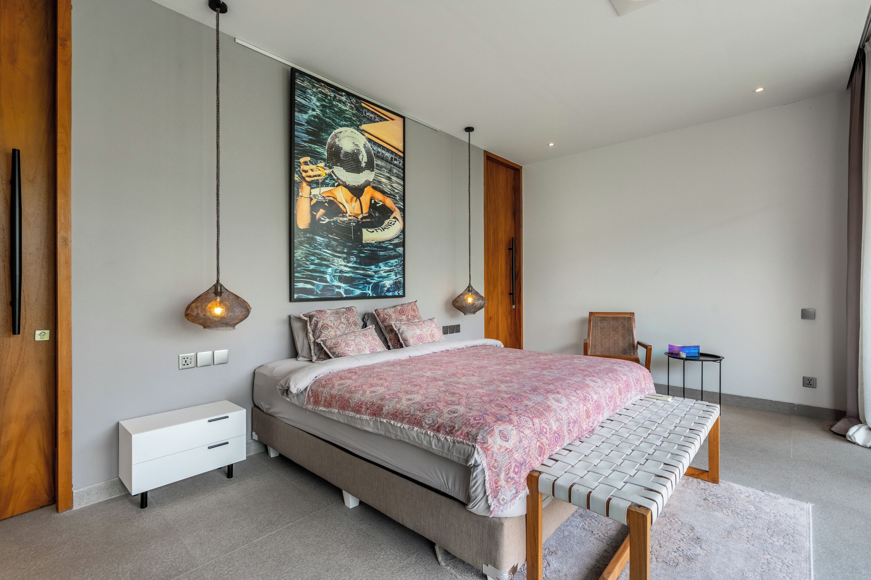 Un dormitorio moderno con una cama grande, mesitas de noche, un banco, un cuadro y lámparas colgantes.