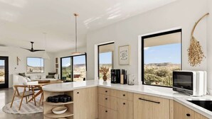 Une cuisine moderne dotée d’un grand îlot central, de meubles en bois et offrant une vue sur le paysage désertique.
