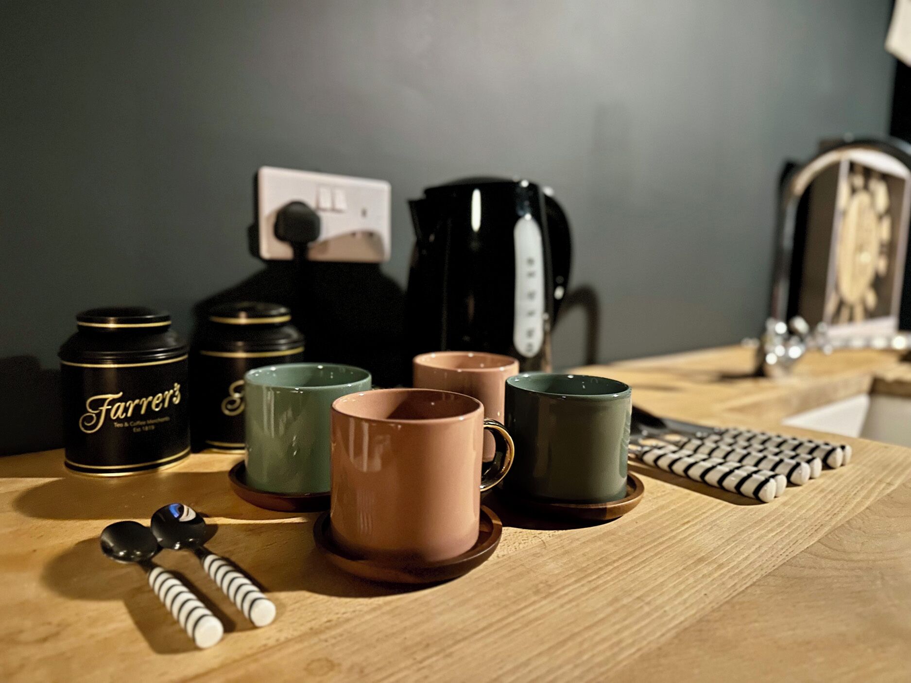 A wooden table with a coffee maker, mugs, and a Farrier's tea & coffee canister.