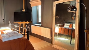 Une chambre à coucher avec un lit, un téléviseur posé sur un meuble, un grand miroir et un radiateur.