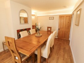 A dining room with a wooden table, white chairs, a vase with flowers, and a wooden door.