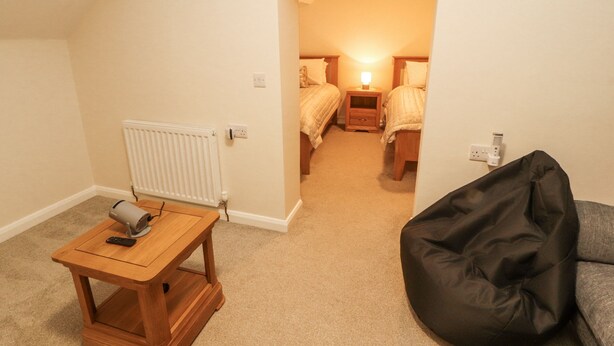 A bedroom with two beds, a bedside table with a lamp, a radiator, and a bean bag chair. - Sun House (Maryport)