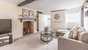 A living room with a fireplace, a round coffee table, a sofa, a TV, and a clock on the wall.
