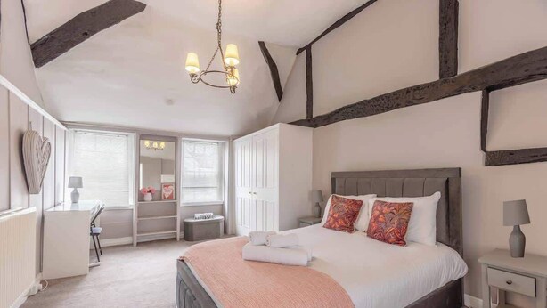 A bedroom with a large bed, a desk, a chair, and a wardrobe.
