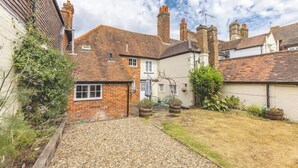 A residential property with a gravel driveway, a small garden, and a brick house with a tiled roof.
