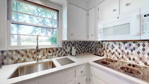 A kitchen with a stainless steel sink, a microwave, and a window with a view of trees. - Charming 2-bedroom cottage on Daffin Park in beautiful Savannah with WiFi, AC (Savannah)