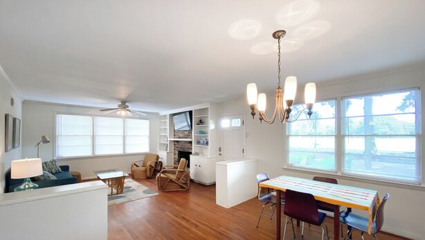 A spacious living room with hardwood flooring, a dining area with a table and chairs, a fireplace, and a ceiling fan. - Charming 2-bedroom cottage on Daffin Park in beautiful Savannah with WiFi, AC (Savannah)