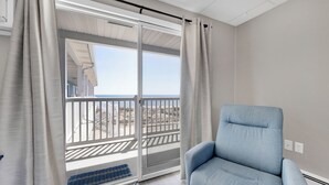 Una habitación con puerta corrediza de vidrio que da a un balcón, un sillón azul y una alfombra pequeña.