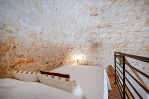 Une pièce avec un mur en pierre, un lit avec une literie blanche et un plancher en bois.