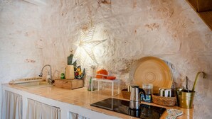 Una cocina con pared de piedra, un lavamanos, una estufa y diversos utensilios de cocina sobre la encimera.