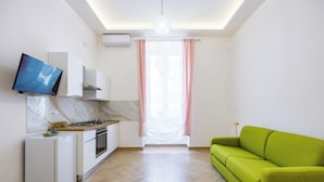 A compact kitchen with a built-in oven, a small refrigerator, and a flat-screen TV mounted on the wall. - Essentia Home (Naples)