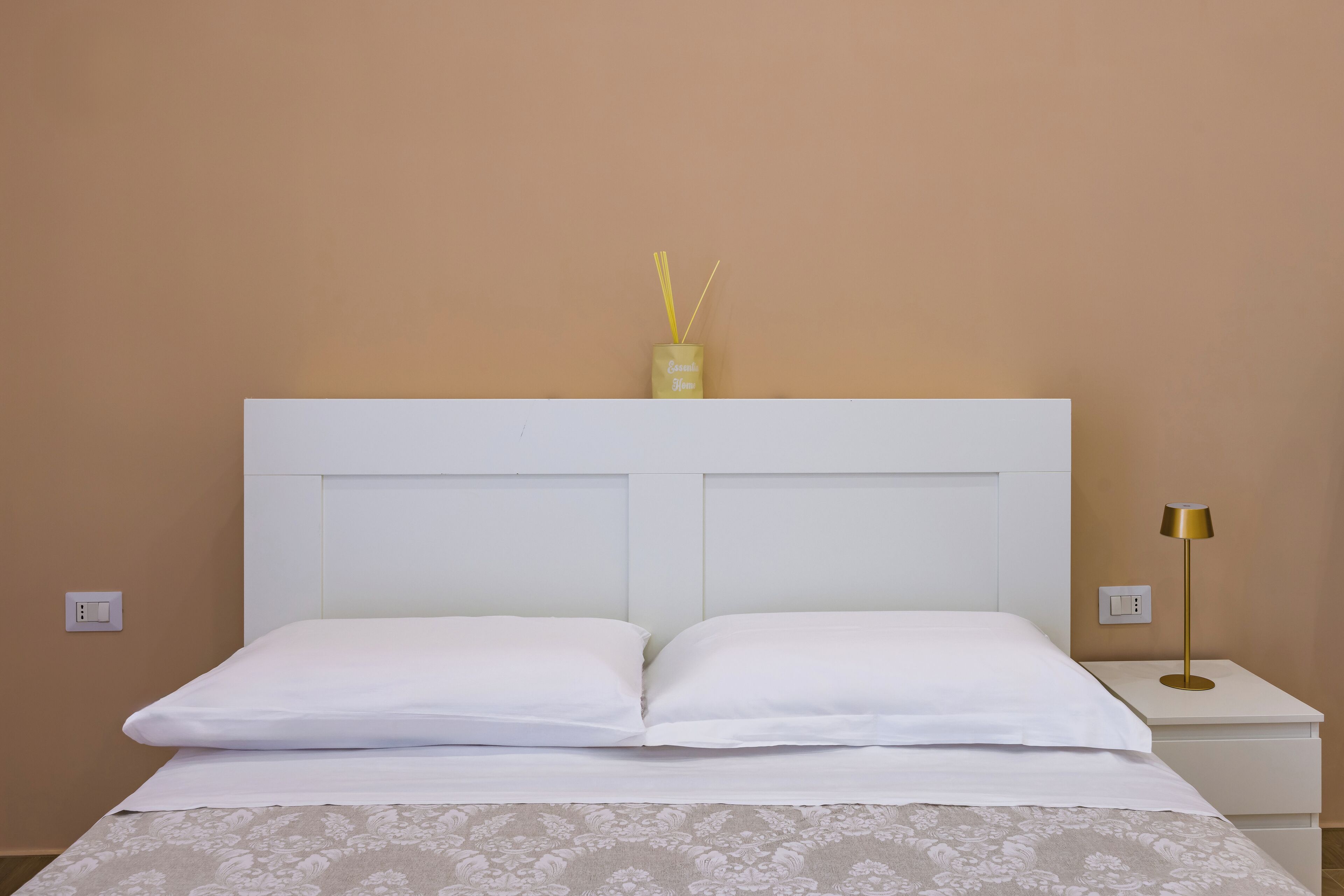 Ein ordentlich bezogenes Bett mit weißen Leinen, ein weißer Kopfseitenverkleidung und ein Nachttisch mit Lampe.