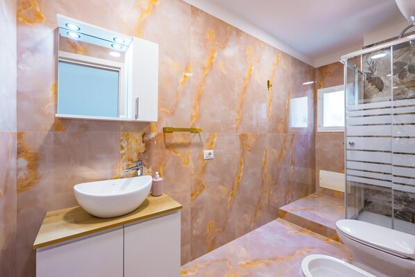 A modern bathroom with a marble backsplash, a white sink, a mirror, and a glass shower enclosure.