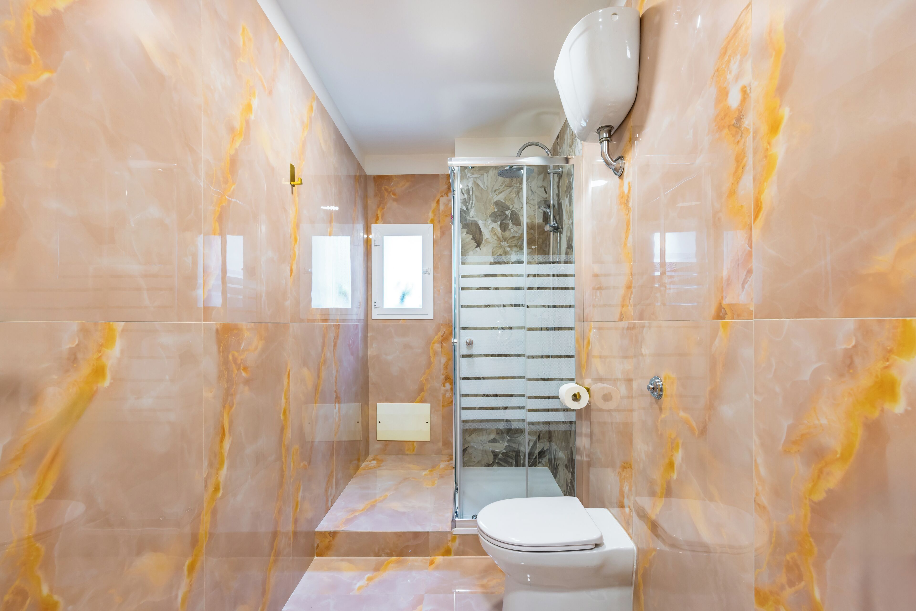 Ein modernes Badezimmer mit einer Glaskabinentrennwand, einer Toilette und Marmorwänden.