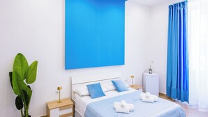 A modern bedroom with a bed, bedside tables, a nightstand, a potted plant, and a large window with curtains. - Essentia Home (Naples)