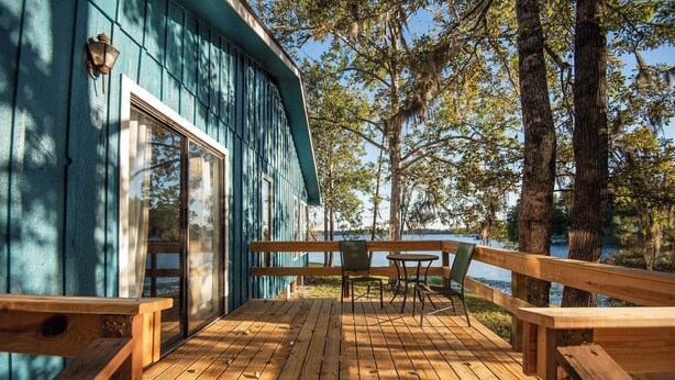 A wooden deck with a table and chairs, overlooking a body of water and surrounded by trees. - Waterfront Lake Retreat • Private Dock & Fire Pit (Anacoco)