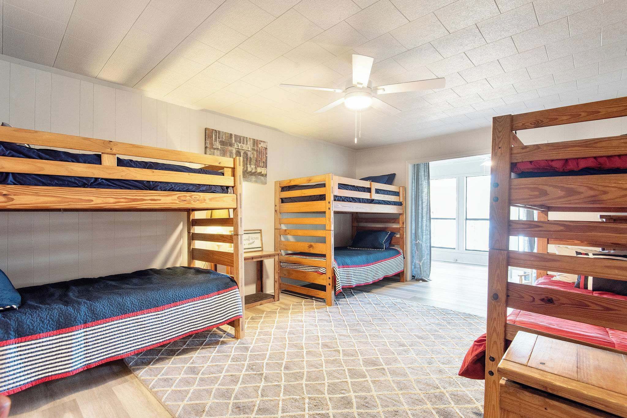 Une chambre de type dortoir, avec des lits superposés, un ventilateur de plafond et une fenêtre laissant entrer la lumière naturelle.