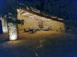 An outdoor seating area with stone walls and a wooden pergola, featuring a sofa and chairs.