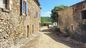 A stone building with arched windows and a gravel path leading to a pool. - Le Mas Tillet (Goudargues)