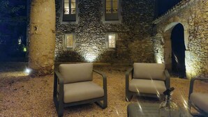 A stone building with wooden beams, two chairs, and a table with a glass object. - Le Mas Tillet (Goudargues)