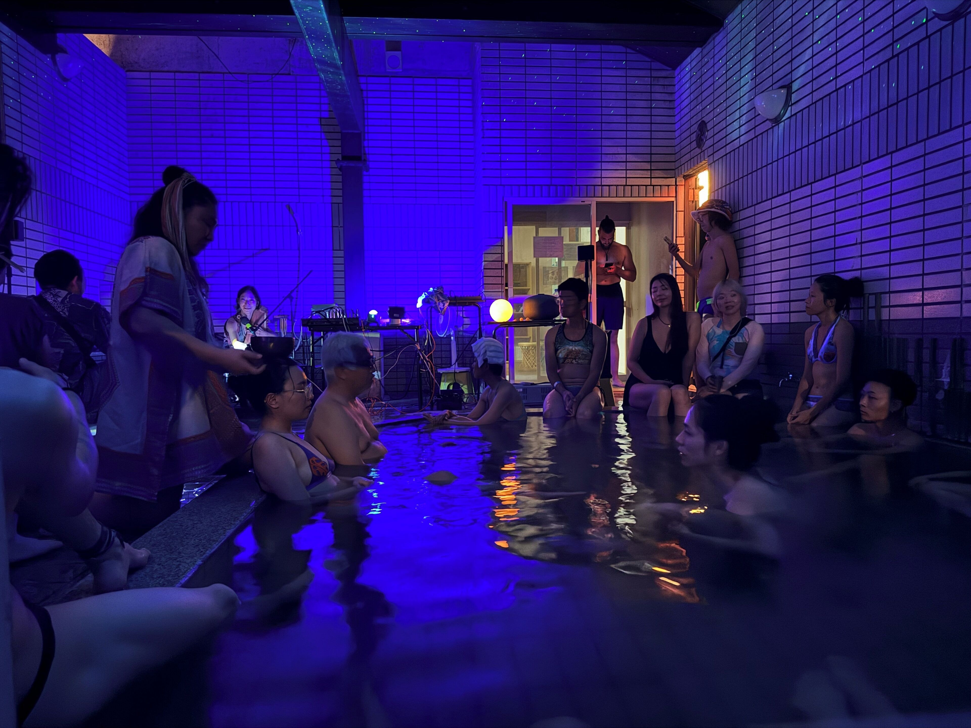 A group of people in a heated indoor pool area with tiled walls and a brick floor.