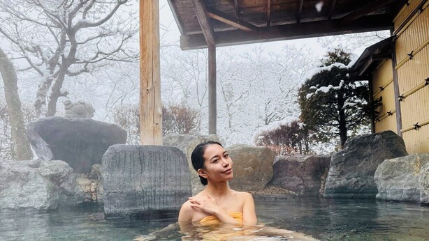 A person in a hot spring surrounded by rocks and a wooden structure. - Sasanoyu (Katashina)