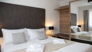 A modern hotel room with a large bed, a wooden headboard, a bedside table with a lamp, and a large mirror.