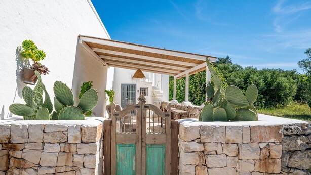 Un edificio blanco con un muro de piedra, una puerta de madera y cactus.