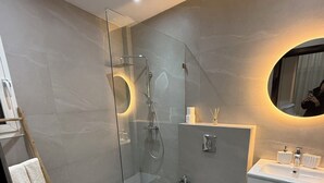 Ein modernes Badezimmer mit einer gläsernen Duschkabine, einem weißen Waschbecken und einem Spiegel mit rundem Rahmen.