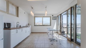 A modern kitchen with a large island, a dining area with a glass table, and large windows offering a city view. - Etna View Superior Flat with Terrace and Jacuzzi (Catania)