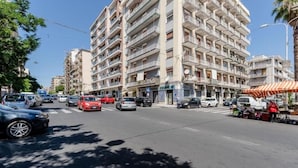 A multi-story building with balconies, a street in front with parked cars, and a small outdoor market on the right. - Etna View Superior Flat with Terrace and Jacuzzi (Catania)