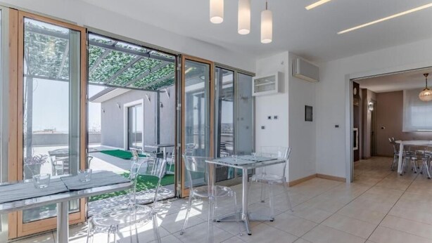A modern interior with glass doors leading to a balcony, clear chairs, and a dining table. - Etna View Superior Flat with Terrace and Jacuzzi (Catania)