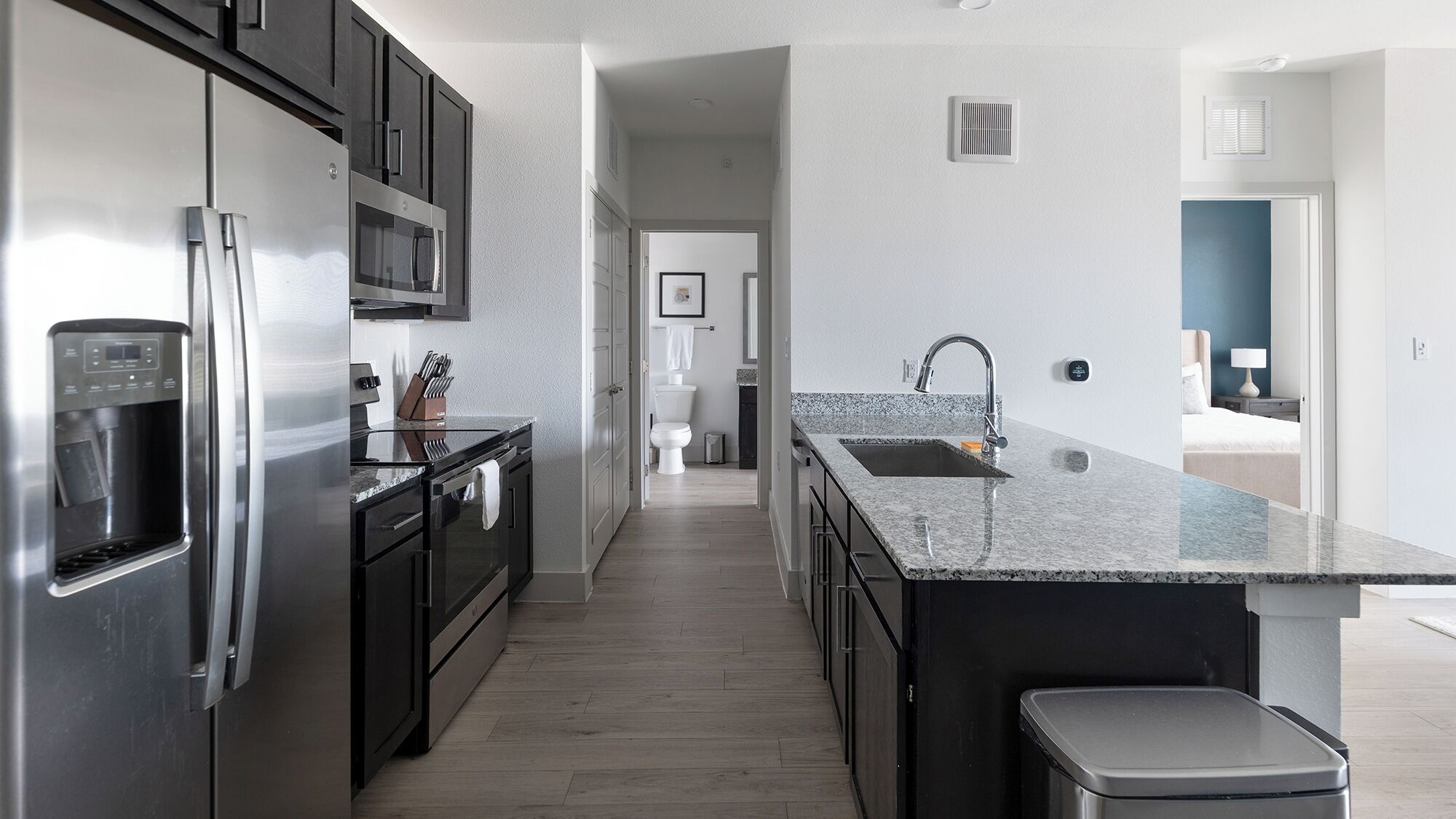 A modern kitchen with stainless steel appliances, a granite countertop, and a view into the adjacent bathroom.