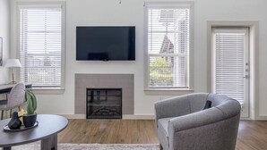 A living room with a fireplace, a television mounted on the wall, and two windows with blinds. - Landing Apartments Waller (Waller)