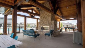 An outdoor patio with a stone fireplace, seating, and a view of a swimming pool. - Landing Apartments Waller (Waller)