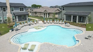 A swimming pool with lounge chairs and a covered seating area, surrounded by residential buildings. - Landing Apartments Waller (Waller)