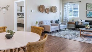 A spacious living room with a round dining table, wicker chairs, a grey sofa, and a ceiling fan. - Phoenix Goodyear Apartments by Landing (Goodyear)