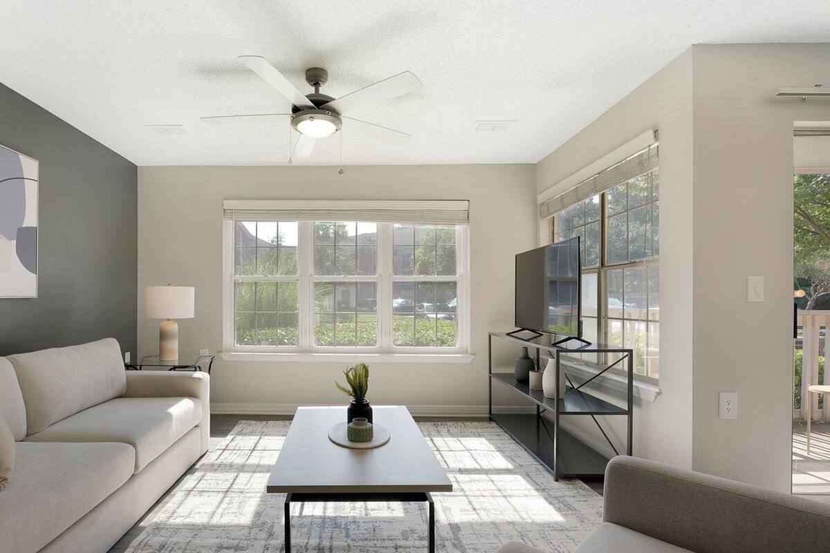 A living room with a sofa, a coffee table, a TV on a stand, and a ceiling fan.