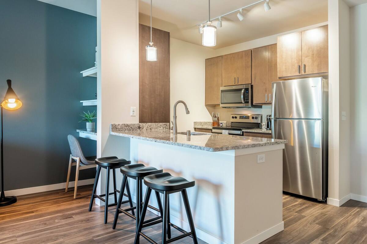 A modern kitchen with a central island, stainless steel appliances, and bar stools.
