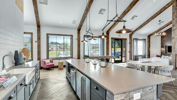 A spacious kitchen with a large island, modern appliances, and a cozy seating area with a pink chair. - Balch Road Apartments by Landing (Madison)