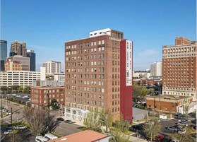 Un edificio de varios pisos con un llamativo letrero rojo vertical en la fachada.