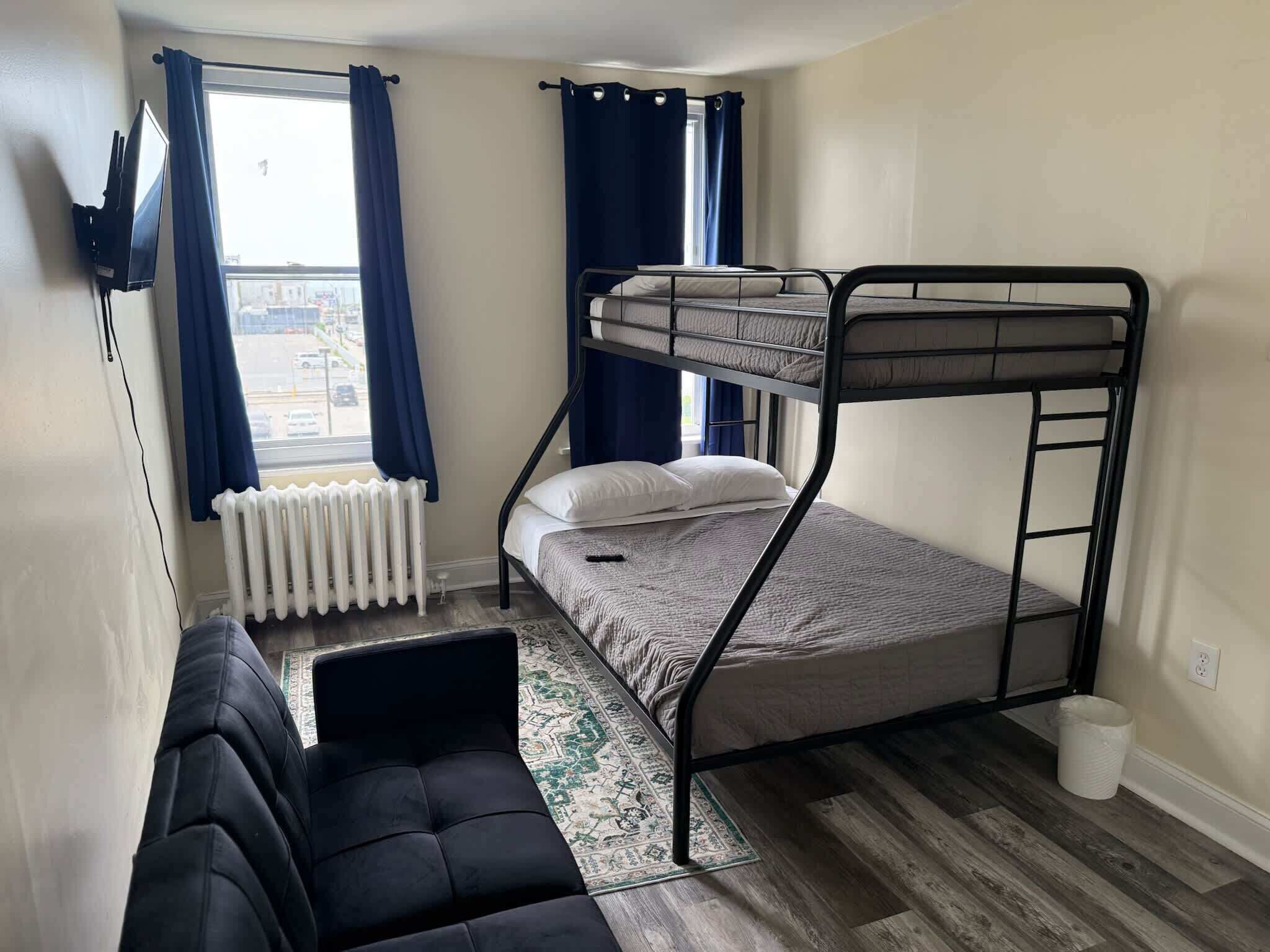 A bunk bed room with a black sofa, a radiator, and a window with curtains.
