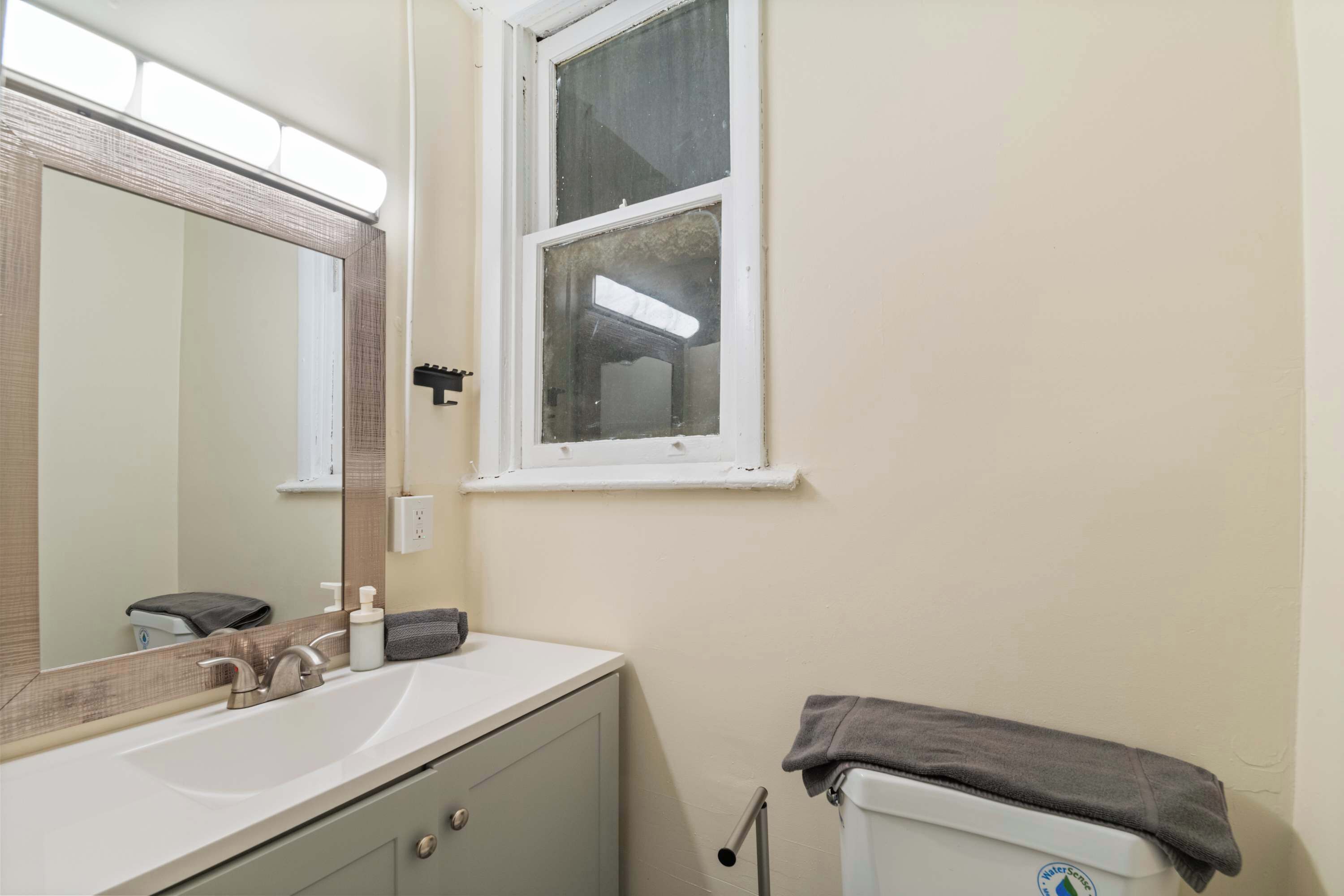A bathroom with a white sink, a mirror, a window, and a towel rack.