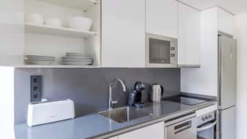 Una cocina moderna con armarios blancos, un lavamanos de acero inoxidable, un tostador, un hervidor, un microondas y un refrigerador.