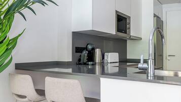 Una cocina moderna con armarios blancos, electrodomésticos de acero inoxidable y una barra con dos taburetes.