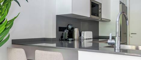 A modern kitchen with white cabinets, stainless steel appliances, and a bar area with two stools.