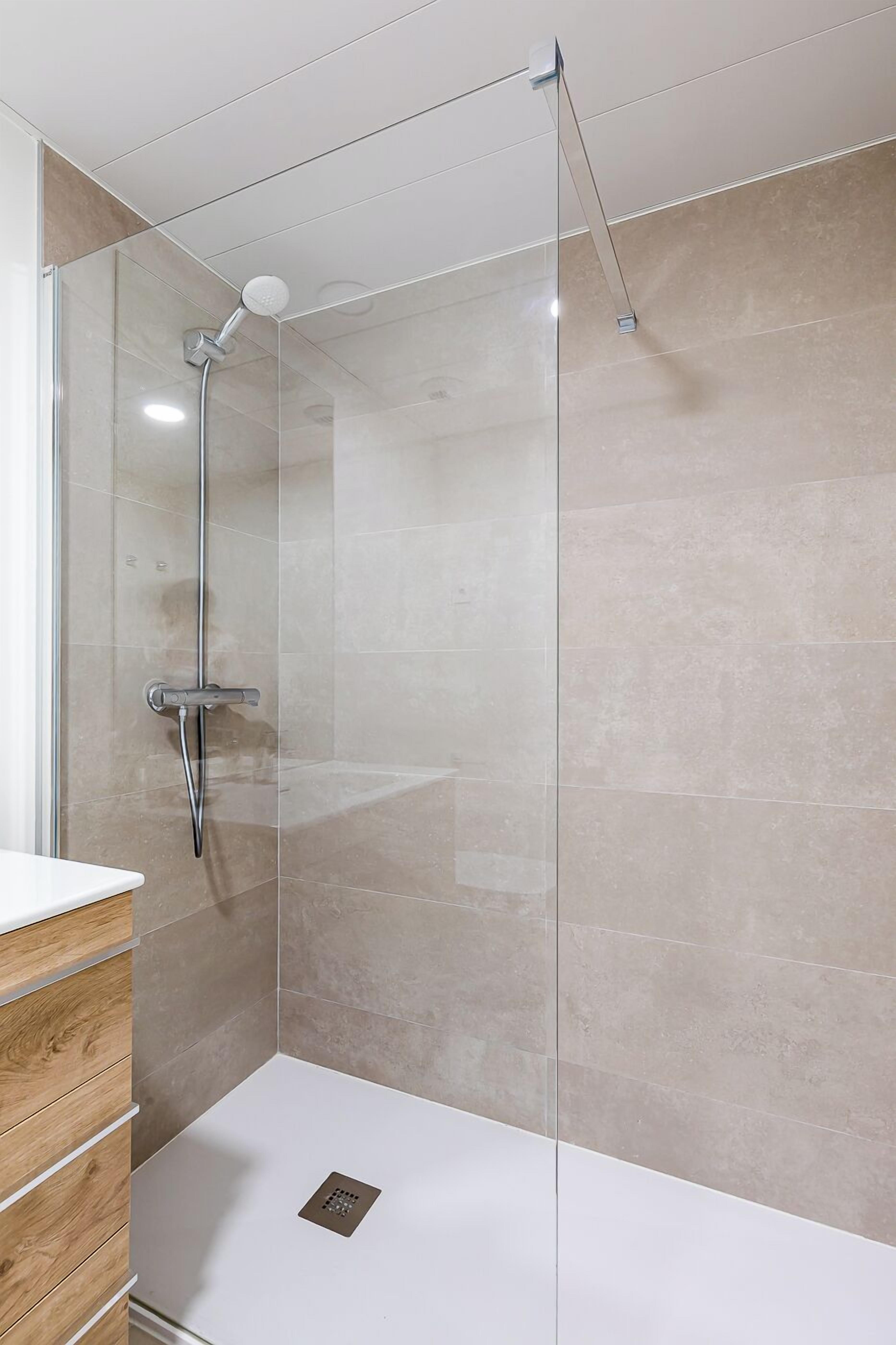Eine moderne Dusche mit Glasabtrennung, einer Handbrause und einem an der Wand montierten Wasserhahn.