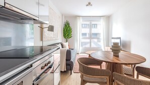 Una cocina moderna con estufa integrada, un comedor con mesa redonda de madera y sillas de mimbre, y un amplio ventanal con cortinas.