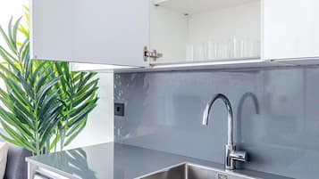 Une cuisine compacte équipée d’un lave-linge intégré, d’un évier en acier inoxydable et d’une étagère en verre au-dessus de l’évier.